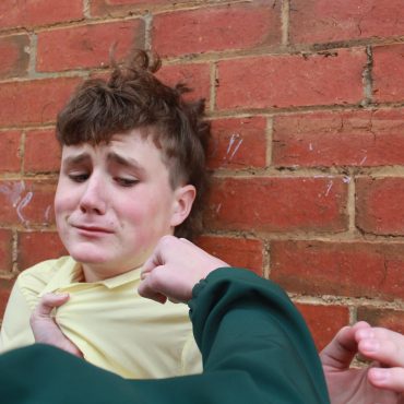 Ein Jugendlicher steht ängstlich an einer Wand. Eine Faust wird ihn gleich treffen.