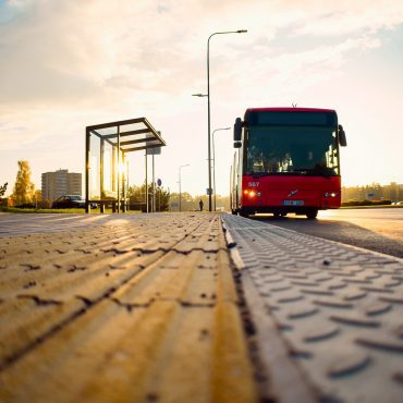 Ein roter Bus im Sonnenuntergang. Links daneben ein Haltestellenhäuschen.